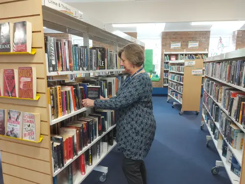 This is an image of a library assistant putting a book back on a shelving unit.