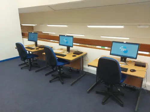 This is an image of three separate tables with computer screen, keyboard and mouse on each.  There is a blue chair in front of each desk.