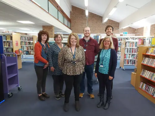 This image has six library staff members standing looking at the camera and smiling.