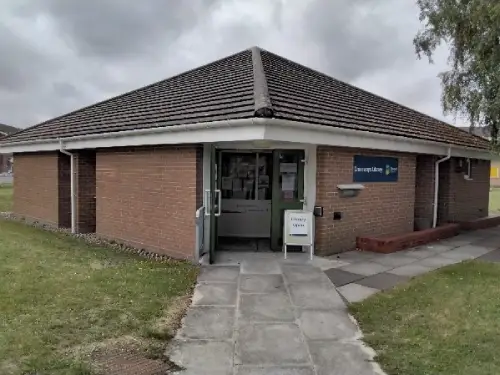 This is an image of the front of Crossways Library surrounded by a grassy area and a cement footpath leading to the door.