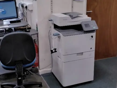 This is an image of a photocopier beside a desk with computer and keyboard.