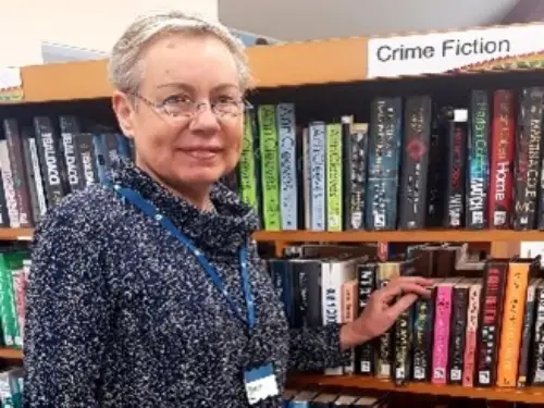 This is an image of a library assistant standing in front of shelves of books.