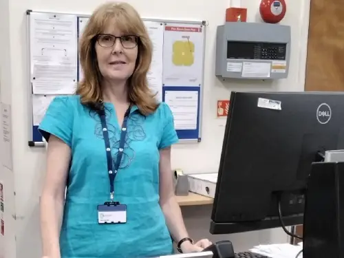 This is an image of a library manager standing behind the front desk with a computer screen and keyboard on the desk.