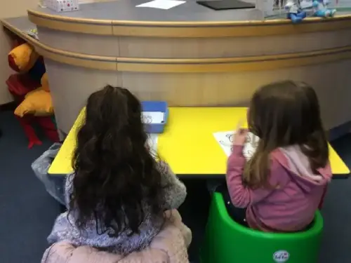 This is an image of two children sitting at a table doing craft activities.