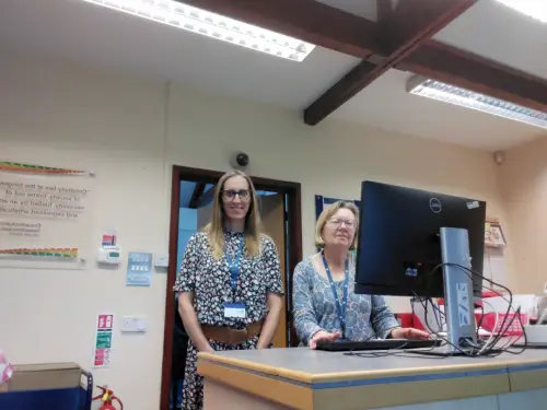 This is an image of two library assistants behind the front desk smiling at the camera.