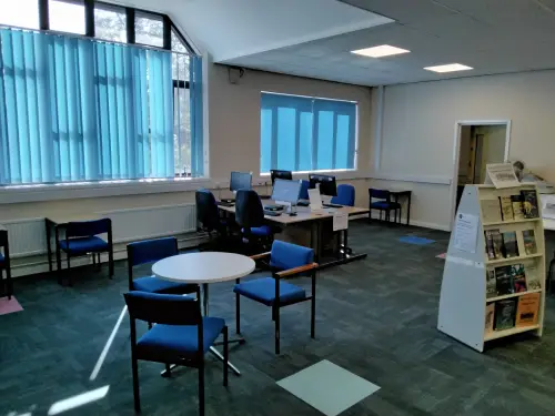 This is an image of computer screens on desks and a small round table and three blue chairs to the foreground.