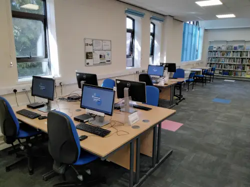 This is an image of desks with computer screens and keyboards and chairs in front.