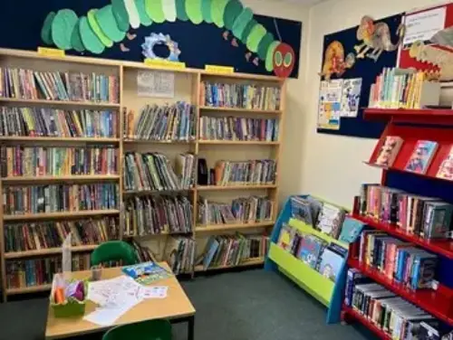 This is an image of the children's area of the library with shelves of books and a small table and chair.