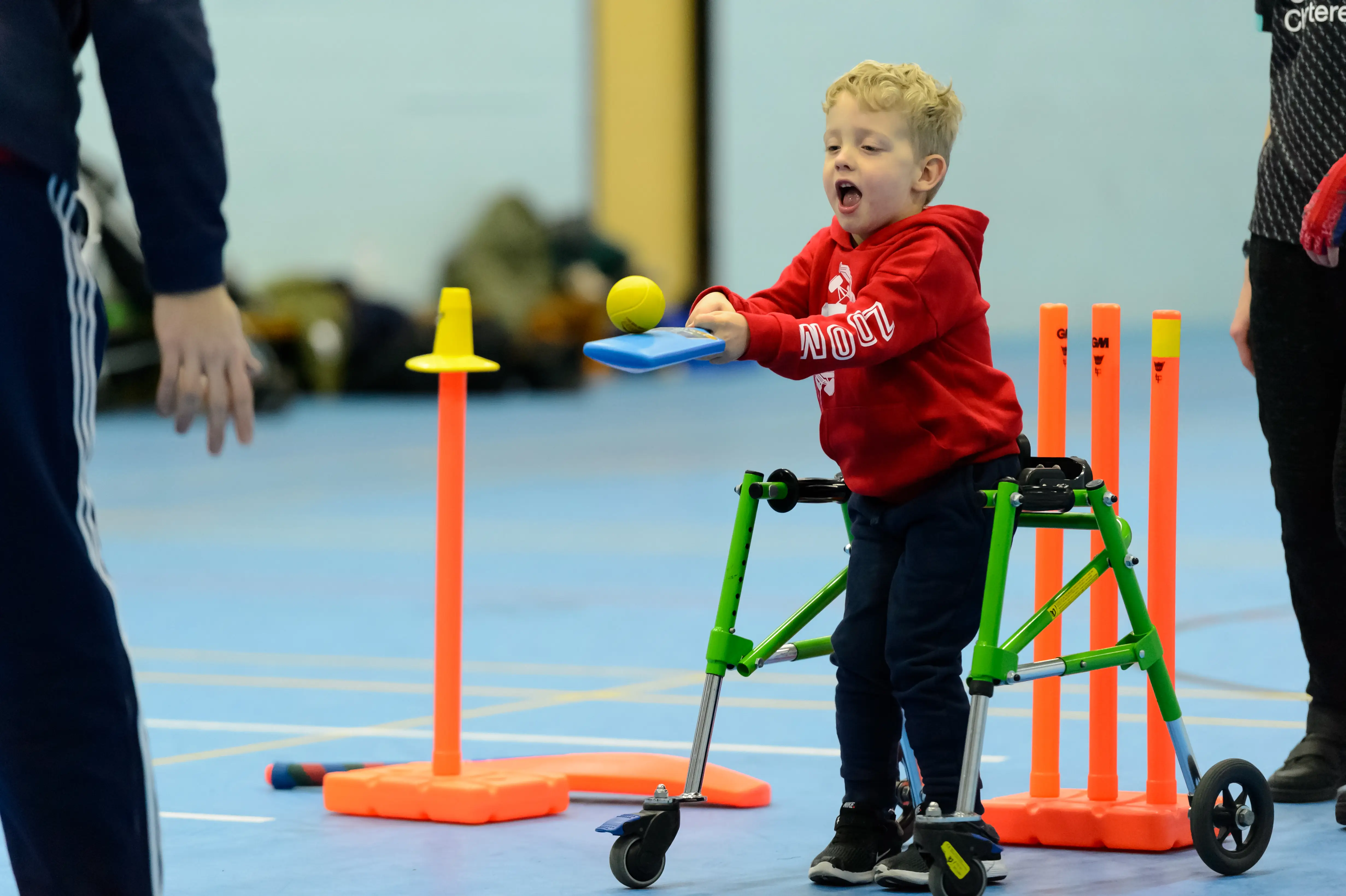 Young boy in a walking frame playing cricket with a post in front of him from which to hit the ball