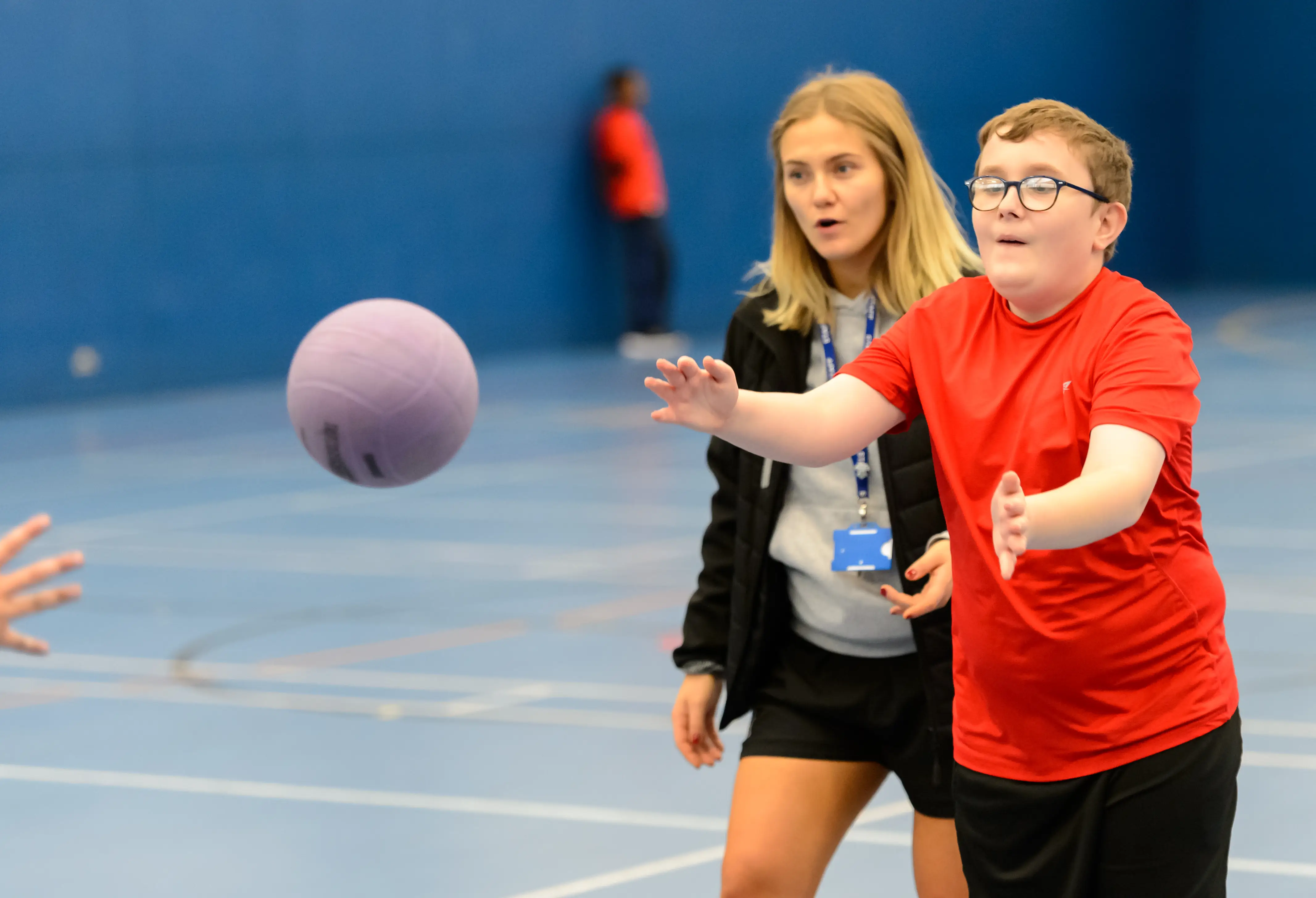 Boy wearing glasses playing basketball with support from an adult