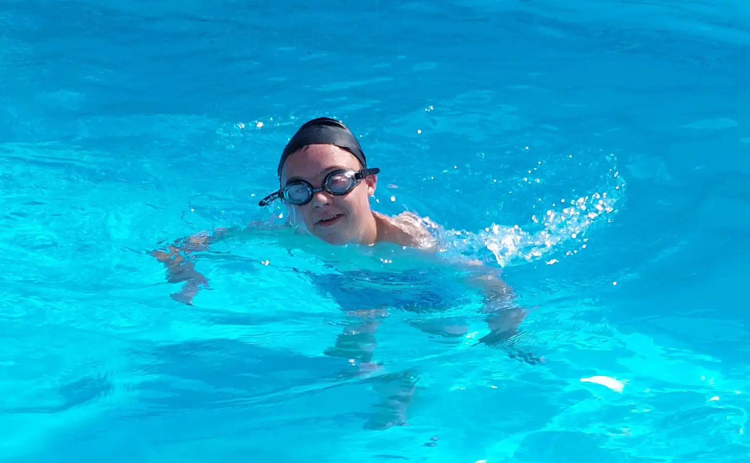 child wearing a black swim cap and goggles in the water