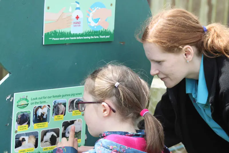 Artz+ Sportz+ female staff member helps a young girl read an information board at a farm