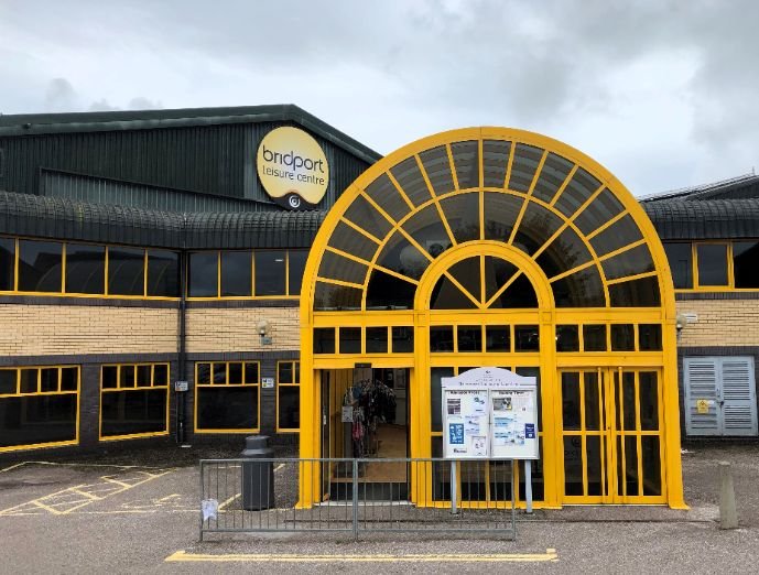 Exterior of Bridport Leisure Centre with yellow and black facade, arched entrance, and visible signage.