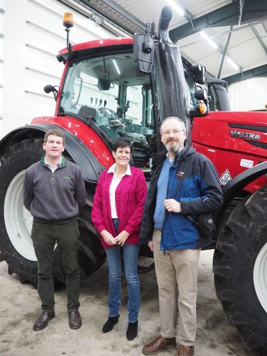 Three people standing in front of a red Valtra tractor inside a workshop at CJ Cox.