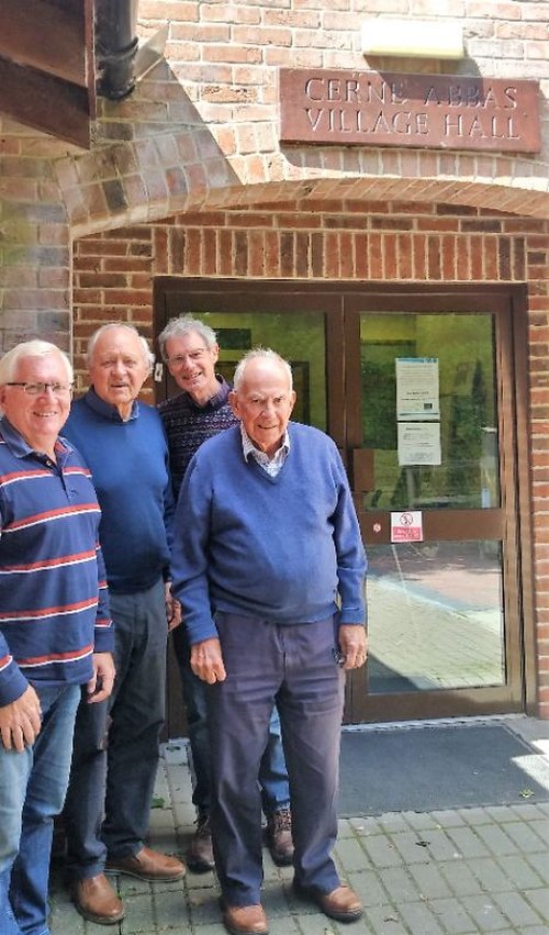 Four people standing in front of Cerne Abbas Village Hall, a brick building with glass doors.