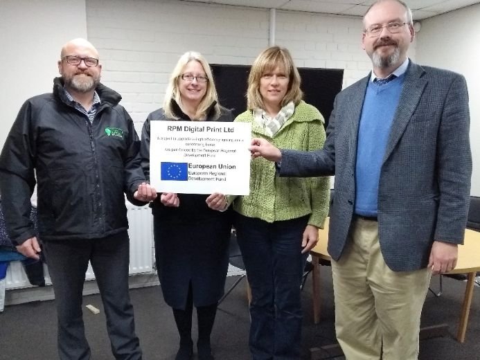Four people indoors holding a sign about RPM Digital Print Ltd’s partnership with the European Regional Development Fund.