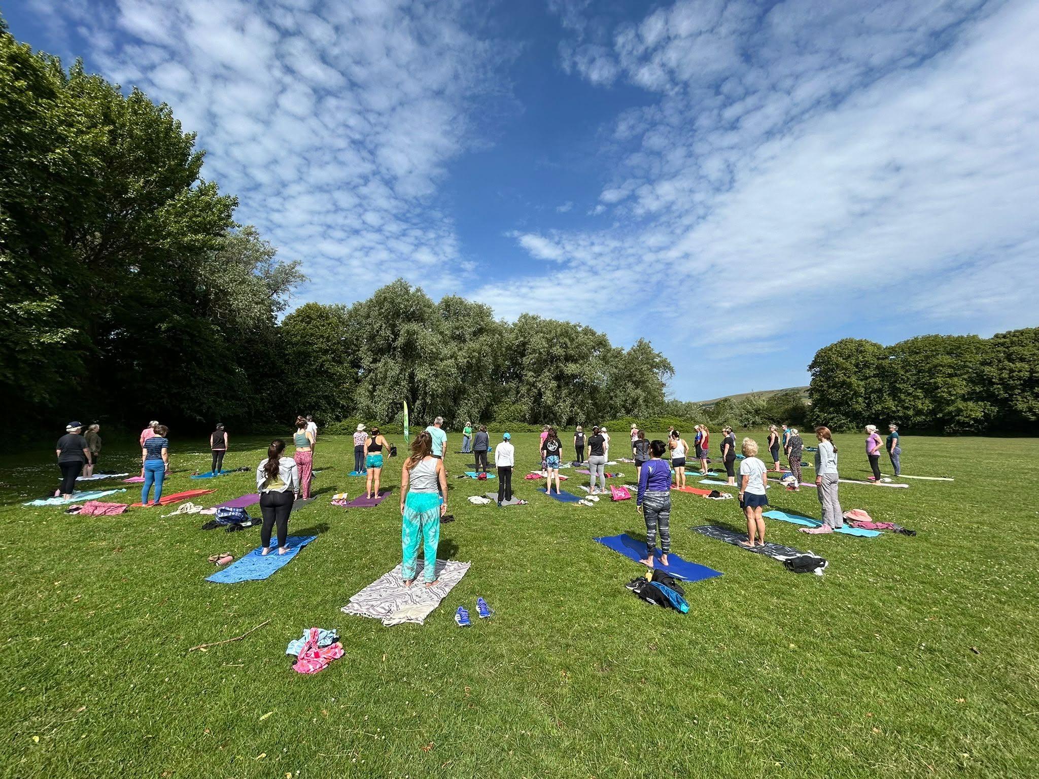 A group of people in a grassy area surrounded by trees standing on yoga mats