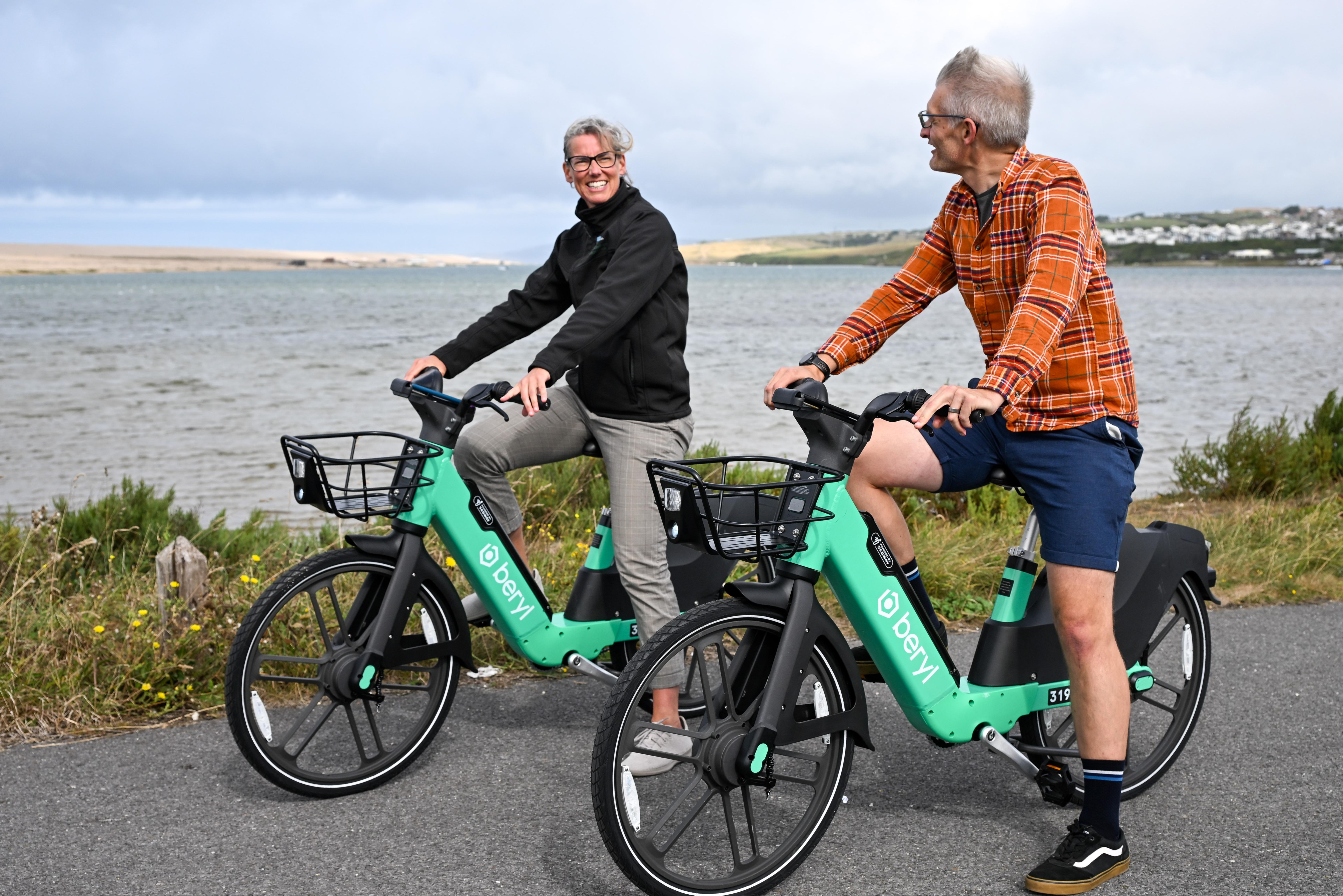 A man and woman smiling at each other while on their e-bikes next to the sea