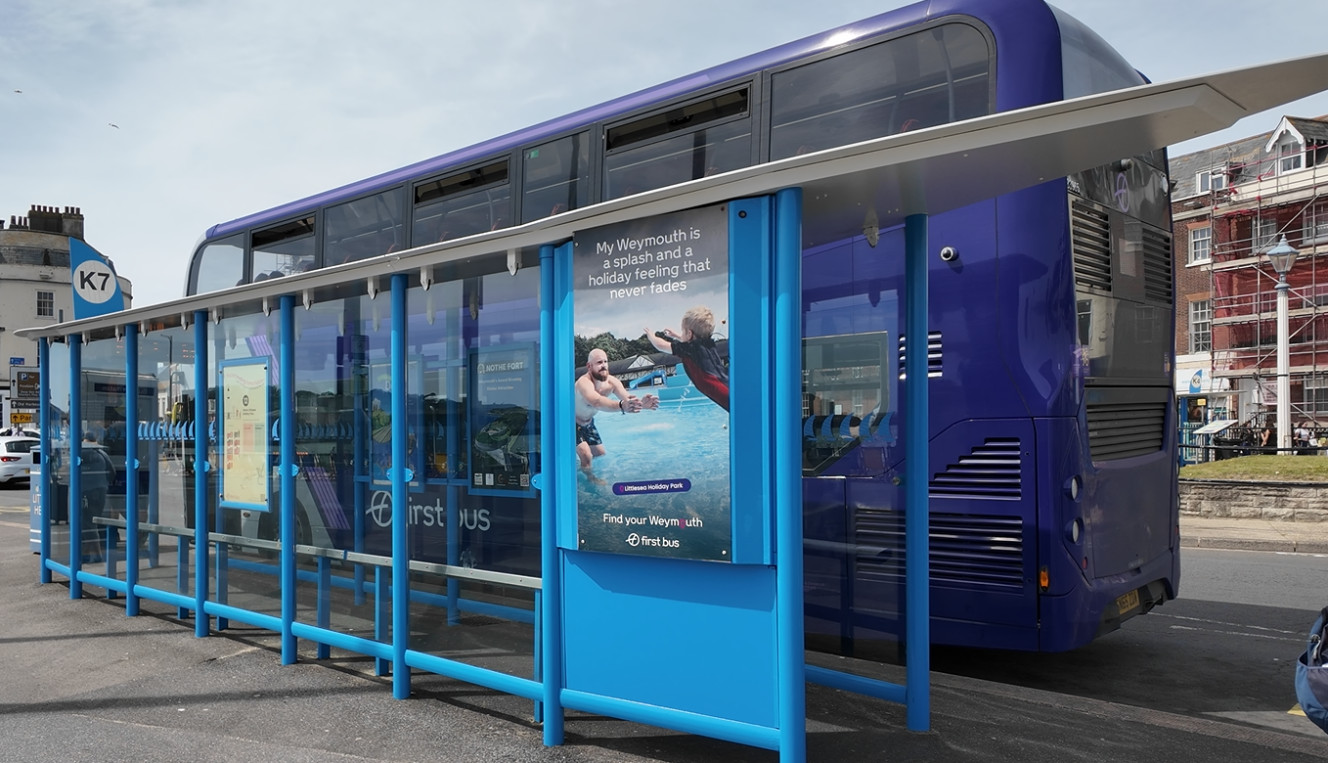 View of refurbished blue bus shelter from the pavement, with a blue First Bus parked next to it.
