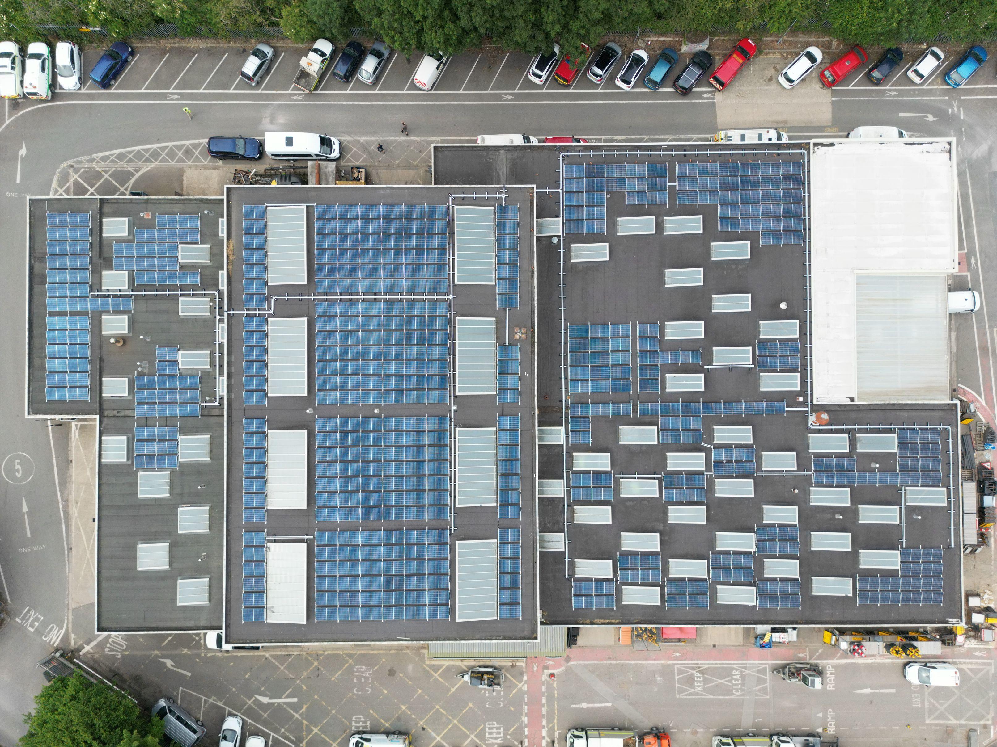An overhead image of the flat roofs of three buildings with solar panels affixed.