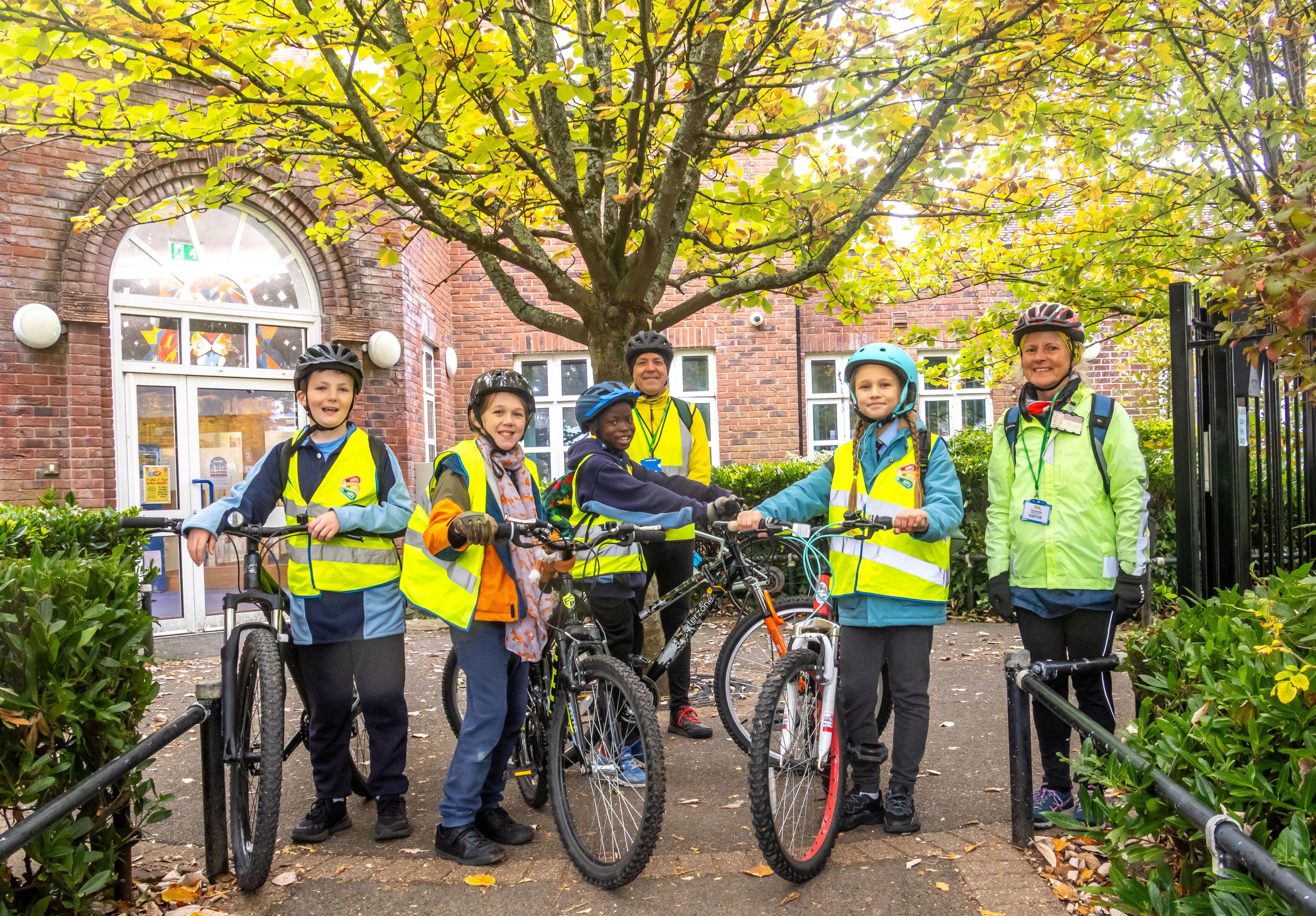Four school children with bikes plus two adults wearing cycle helmets