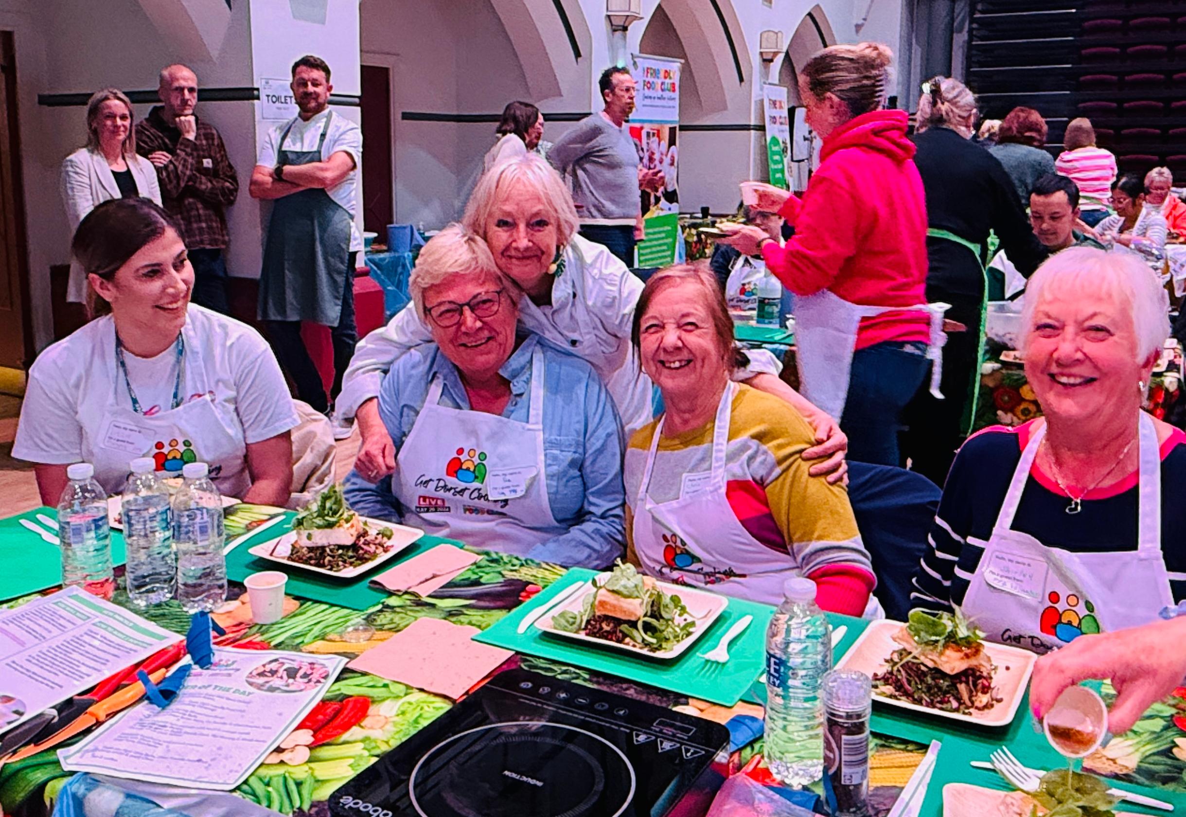 A group of people smiling at the camera with their plates of prepared food in front of them