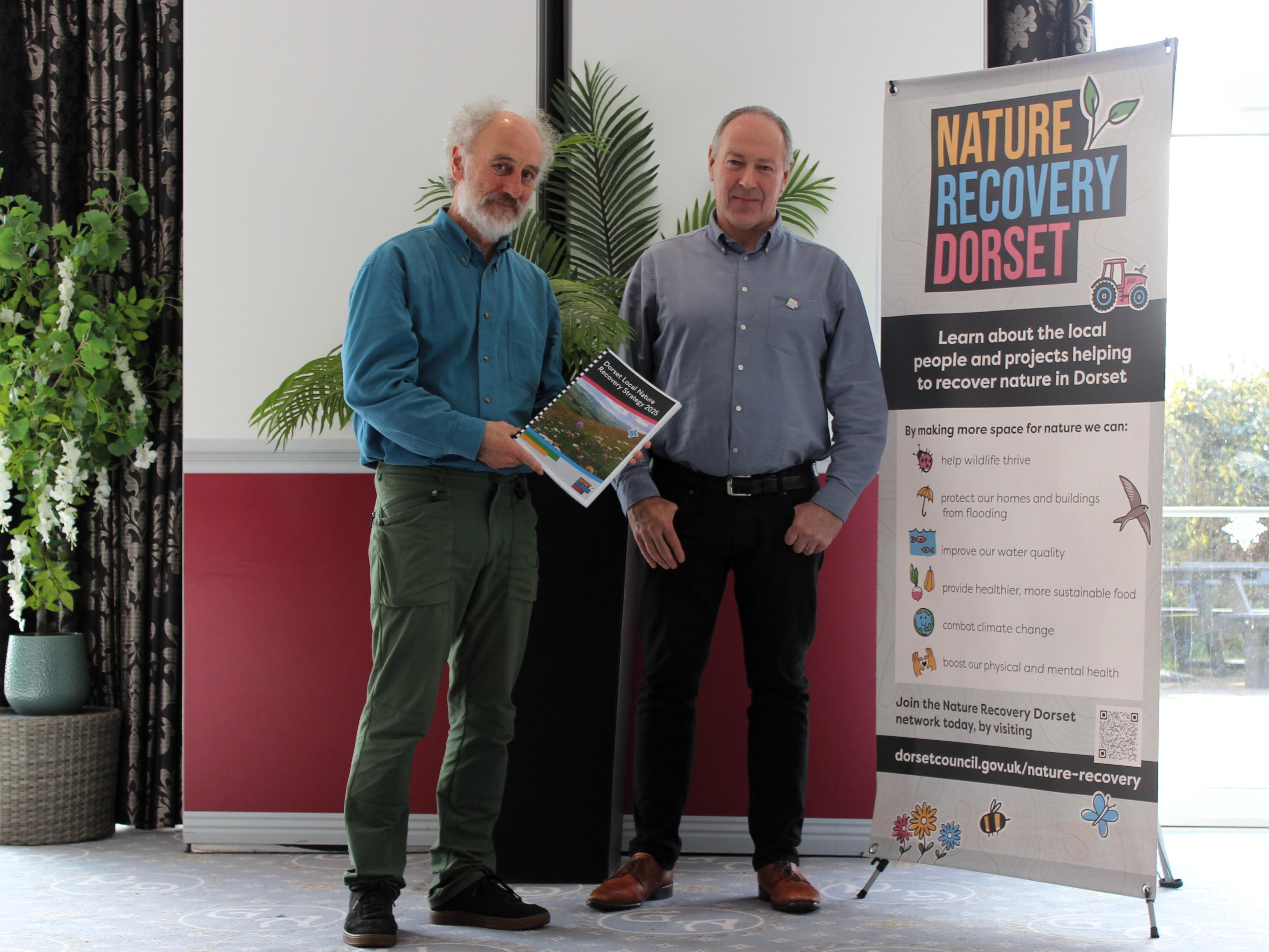 Two men standing in front of a sign that says Dorset Local Nature Recovery Strategy