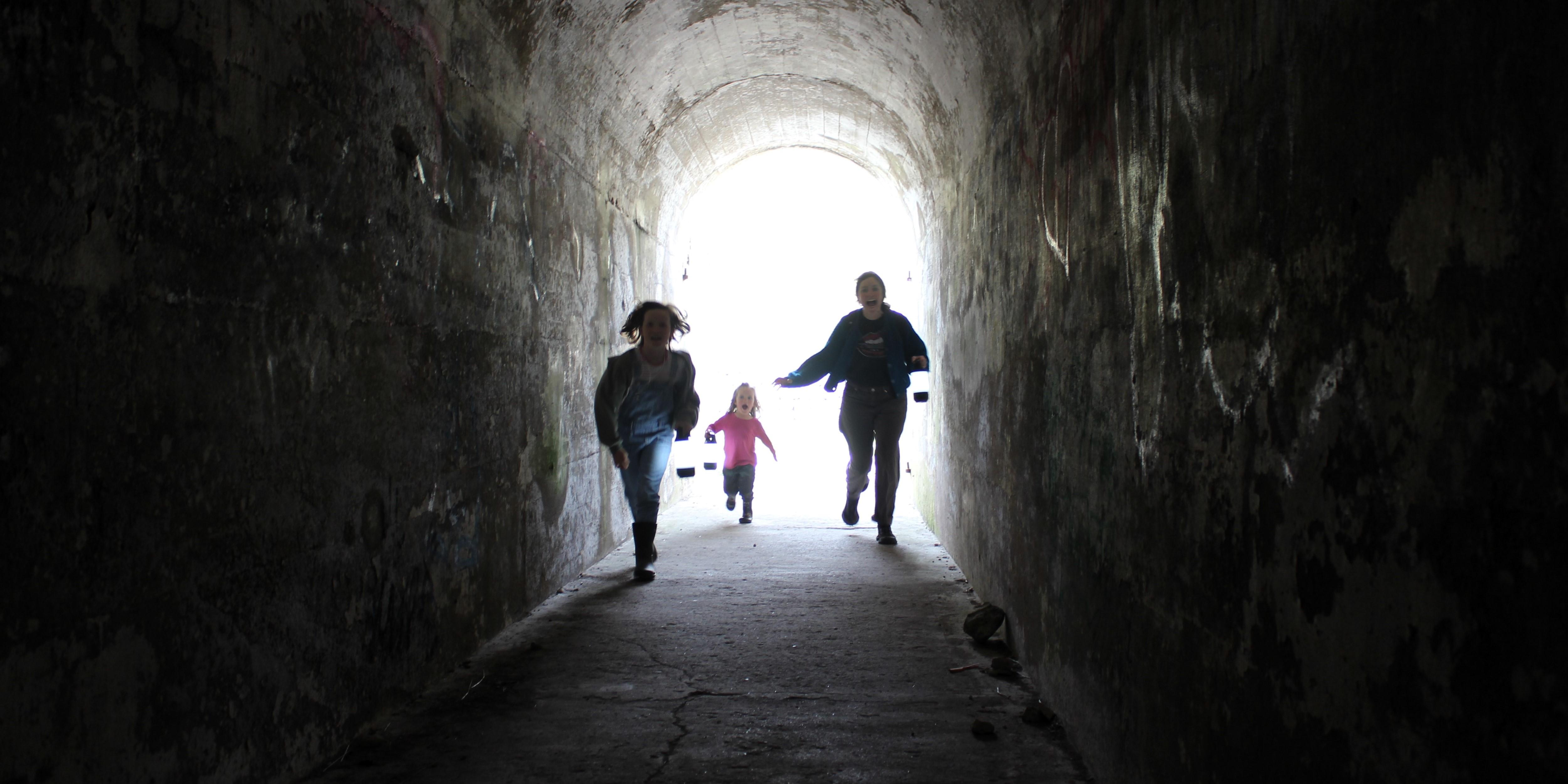 an adult and two children run through a dark tunnel