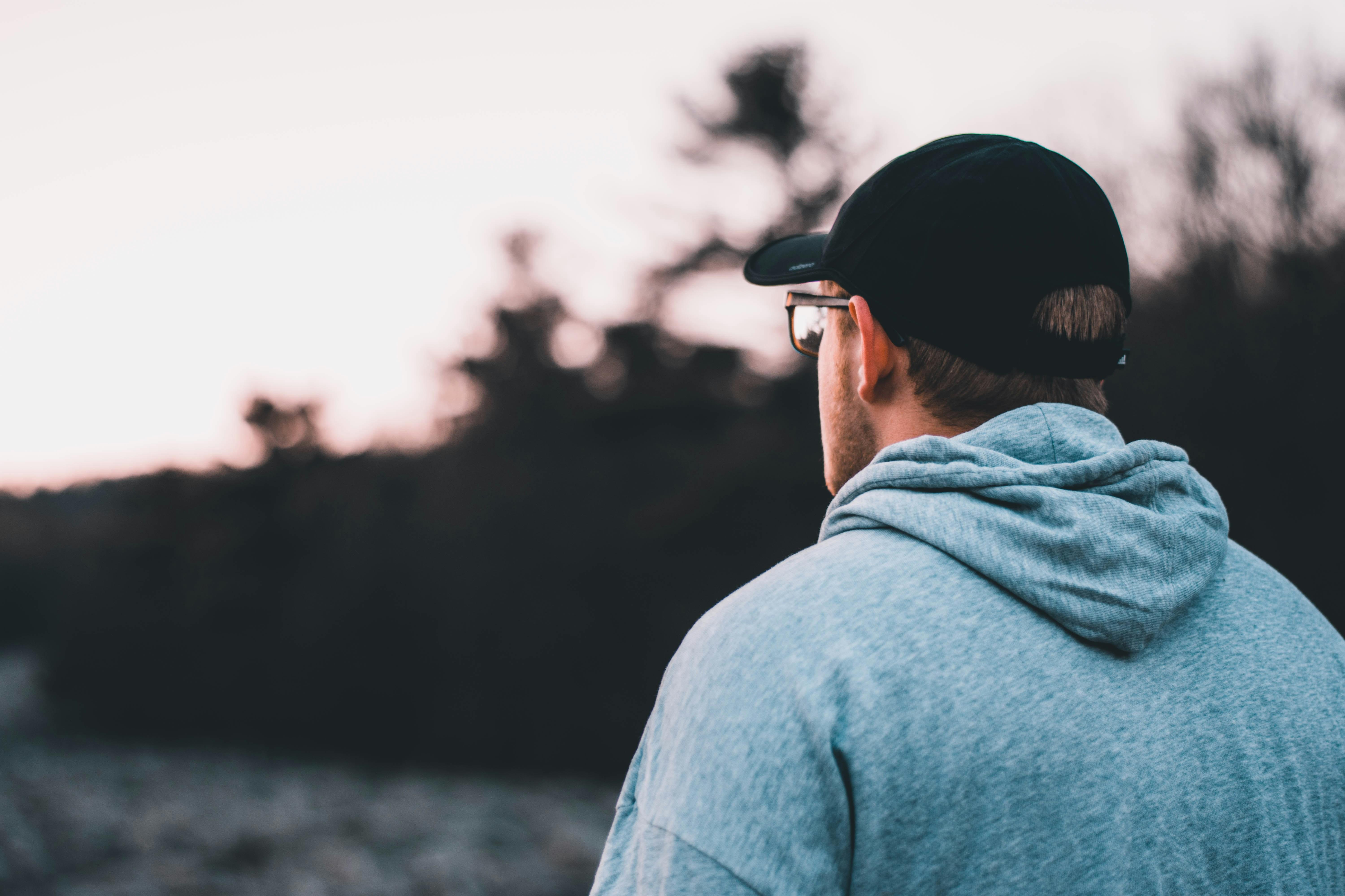 A stock image of a man looking into the distance, he is wearing a hat and glasses and a grey top