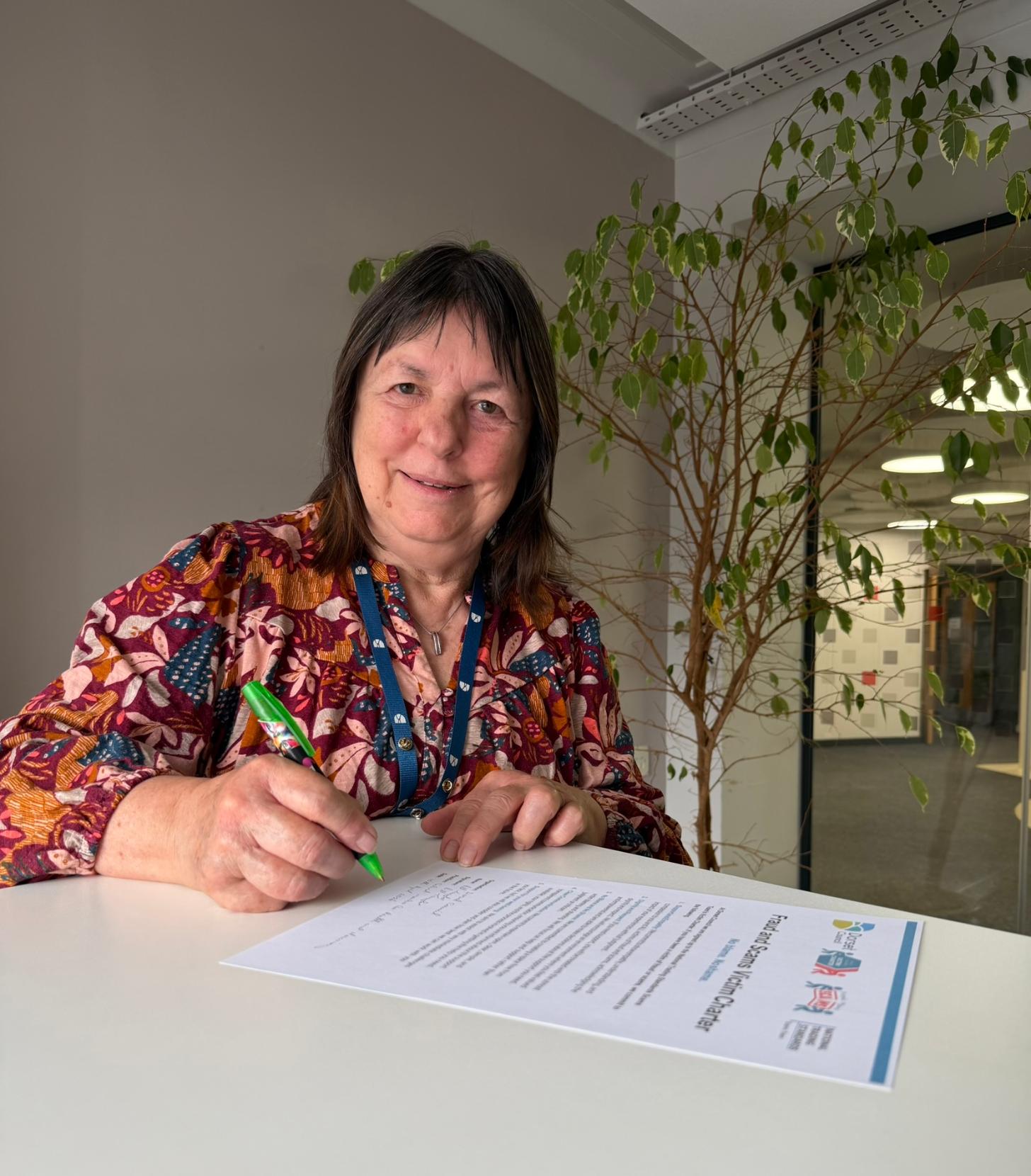 Cllr Gill Taylor holding a green pen to sign the Fraud and Scams Victim Charter
