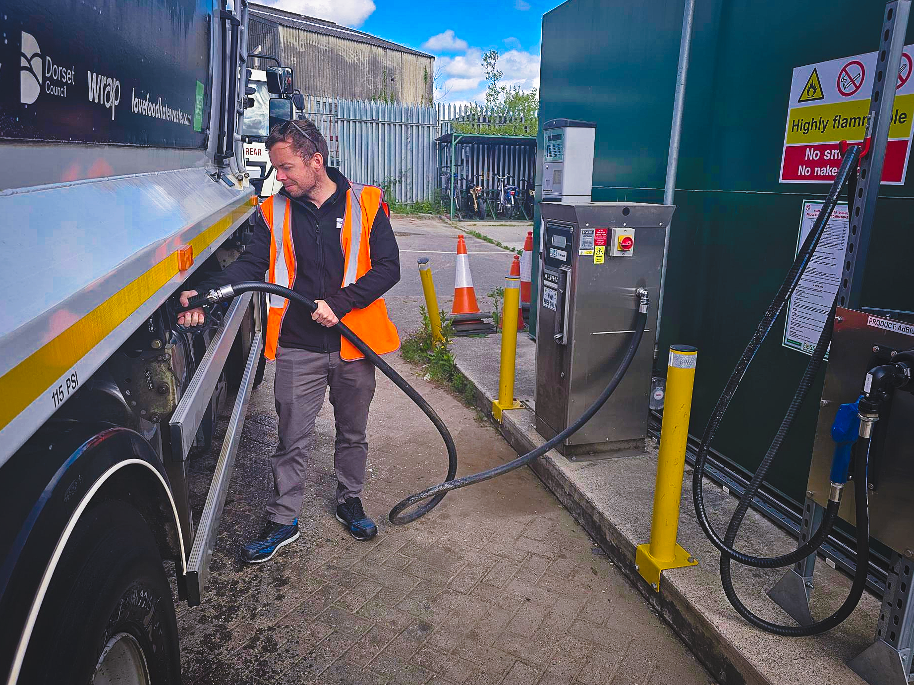 A person wearing an orange high visibility jacket filling a large vehicle with hydrotreated vegetable oil