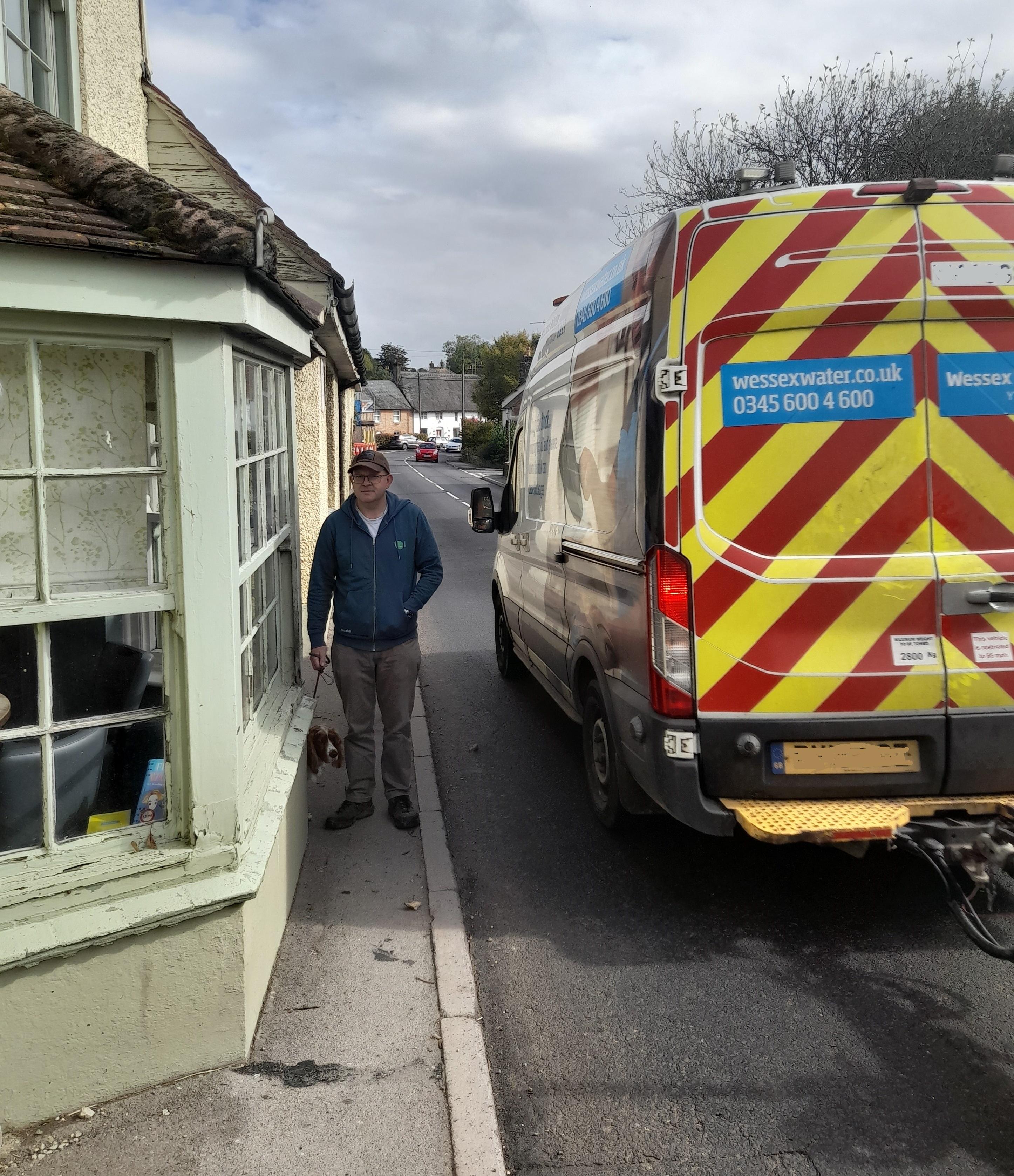 A man with his dog walking along a footway as a vehicle passes them