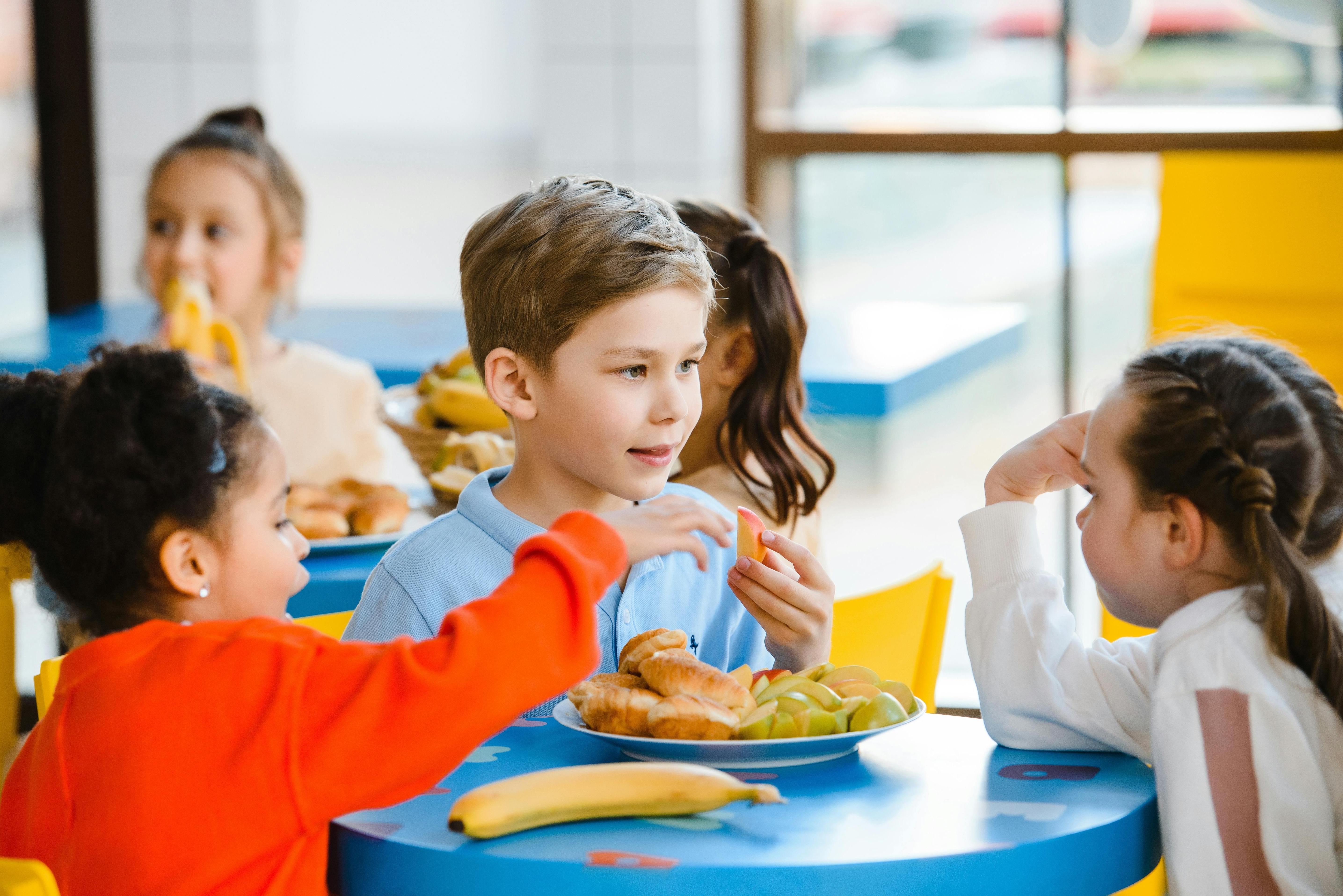 children eating fruit and pastries seated at a table