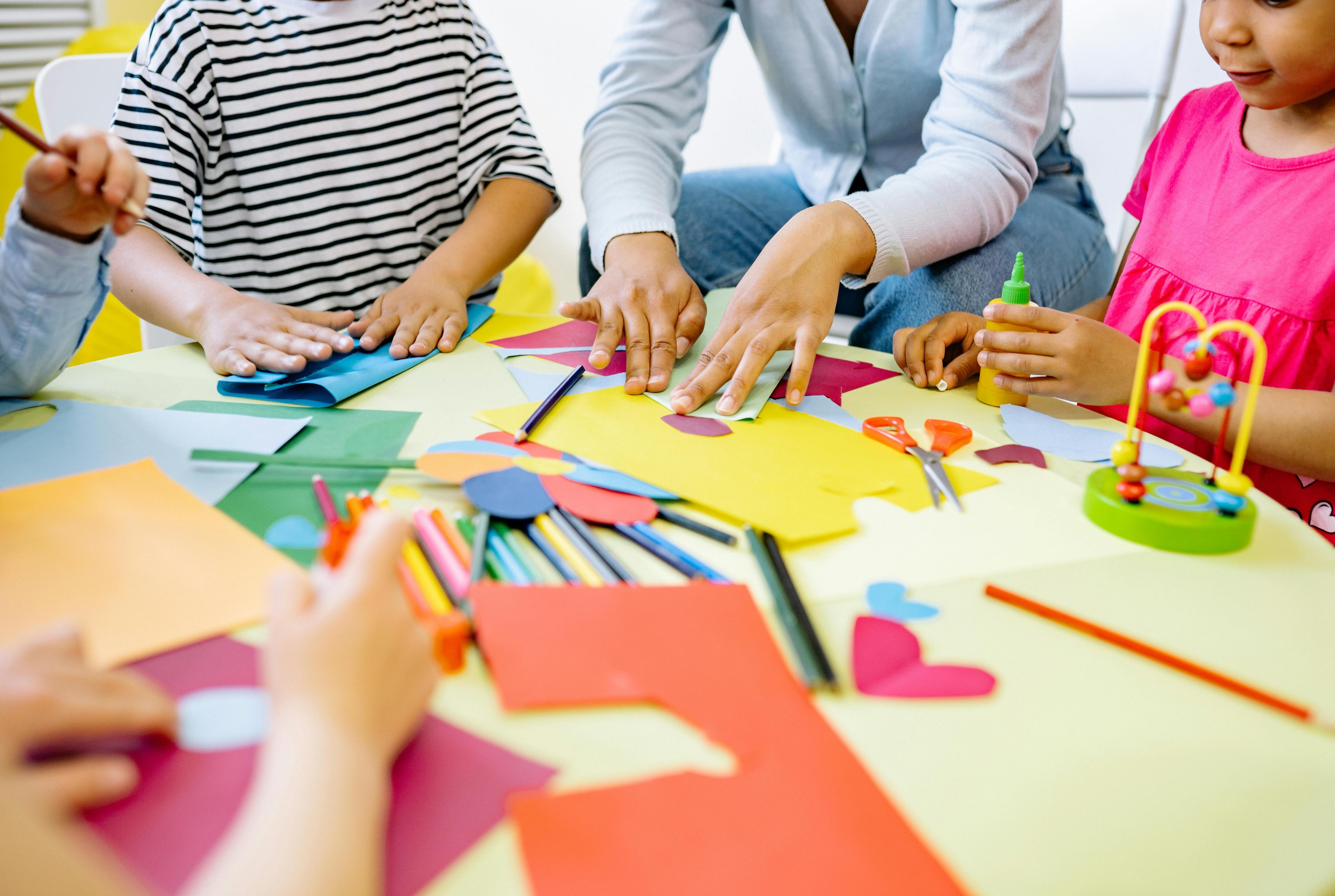 Children's hands at a table, cutting out and gluing coloured paper