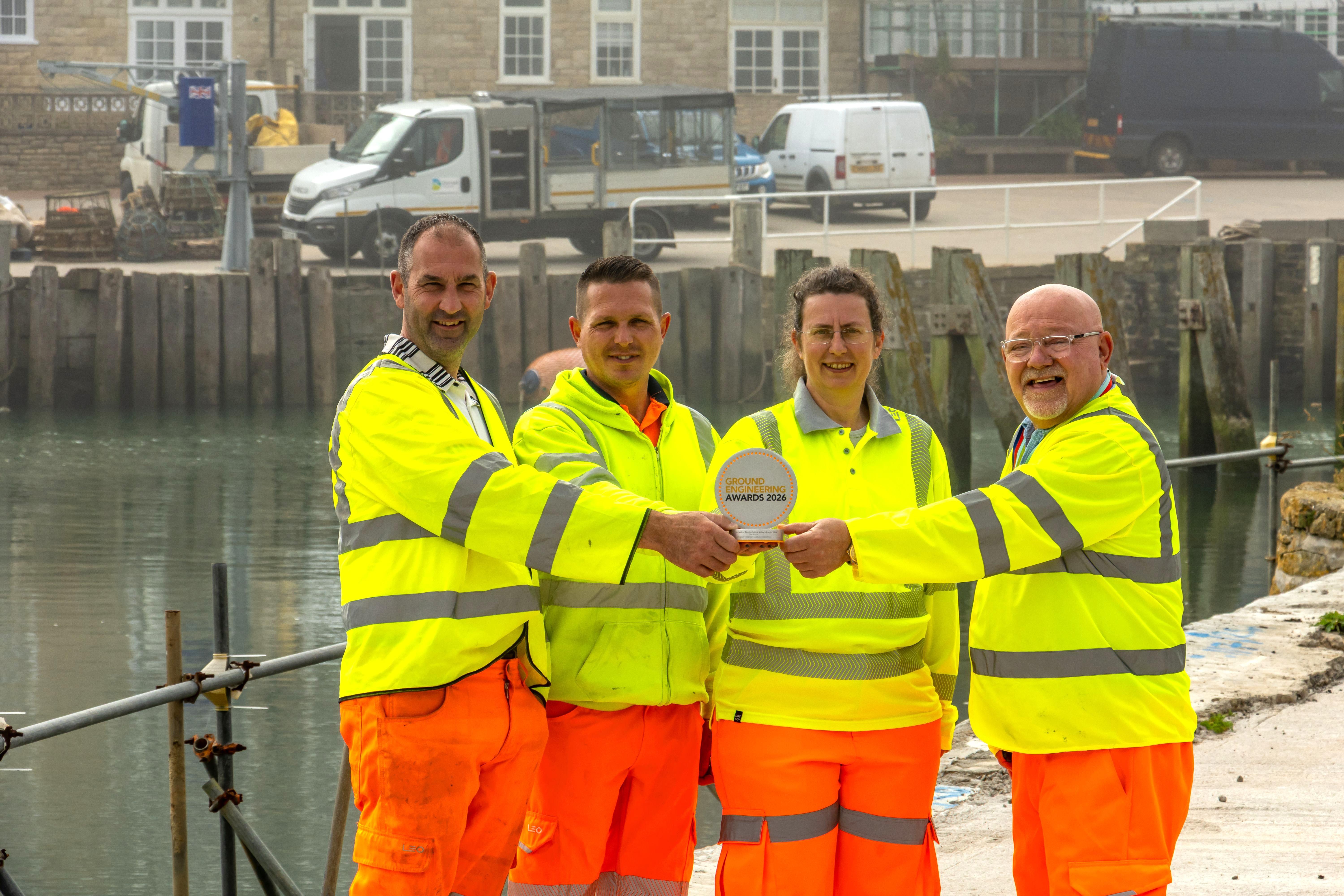 Four people wearing high viz in front of a harbour scene