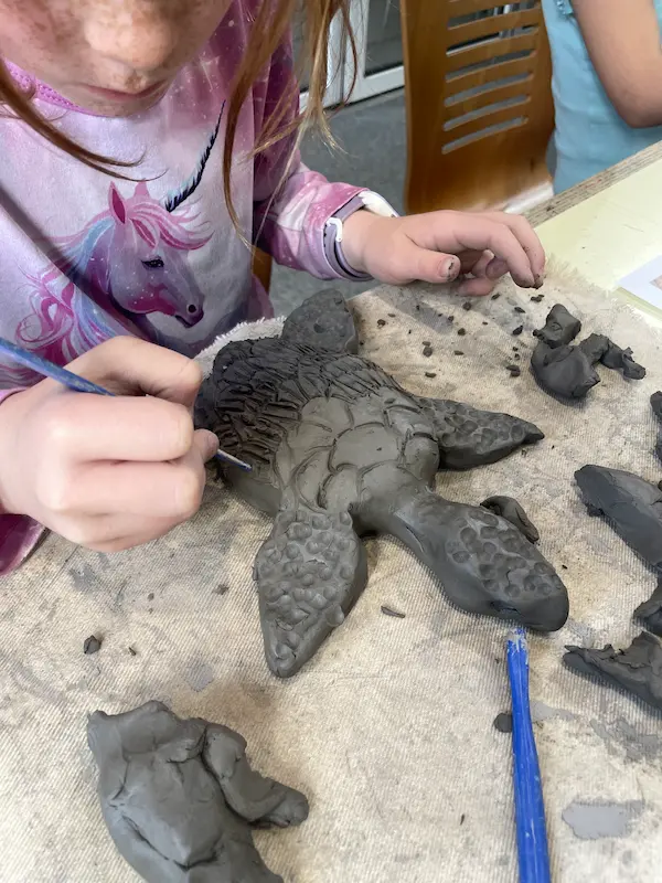 Picture of a girl giving detail to a clay turtle