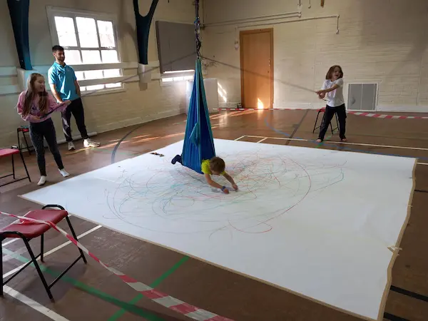 picture of a particpant in a hammock swinging over, and drawing on a big canvas