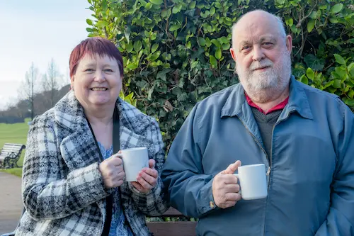 A couple standing outside and drinking from mugs