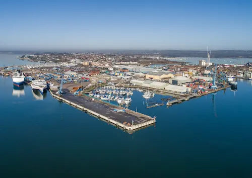 Aerial view of Poole Port showing docks, ferries, marina berths, industrial buildings and quaysides surrounded by coastal waters and the town beyond.