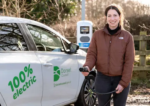 An electric vehicle parked and charging at the village hall in Cerne Abbas, Dorset, illustrating the integration of modern transport in a rural setting.