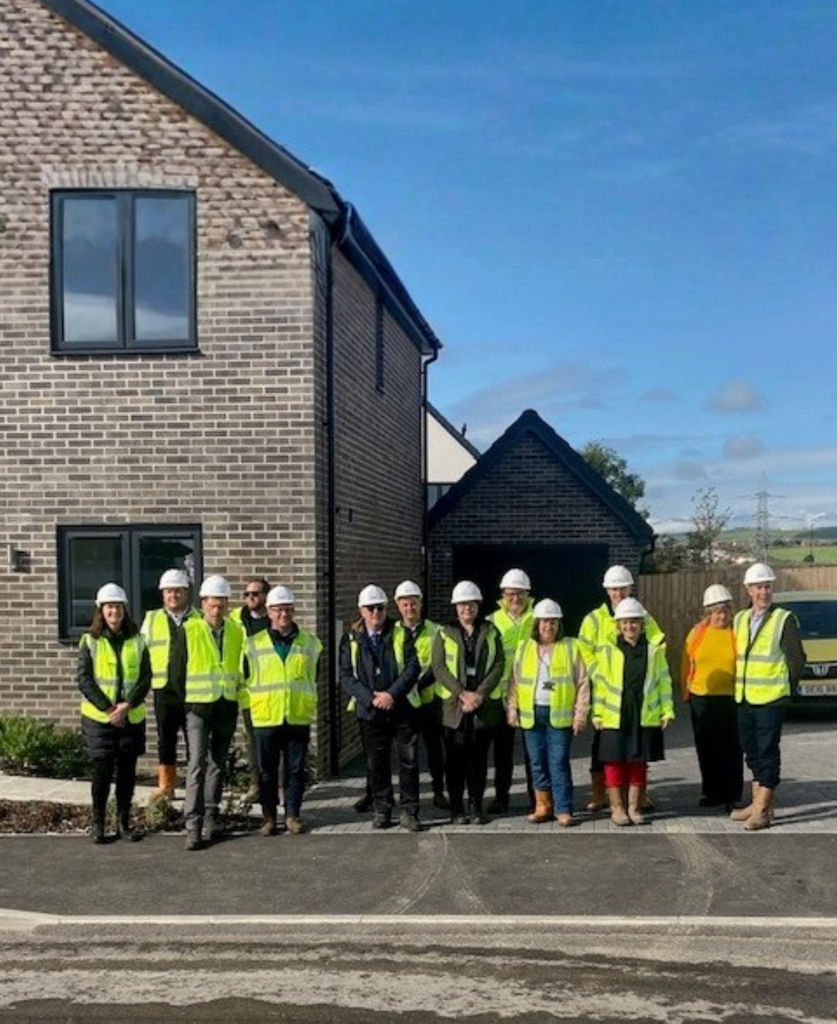 Team of colleagues wearing hi vis jackets and white hard hats stood outside a newly developed property at Bincombe Park, Weymouth