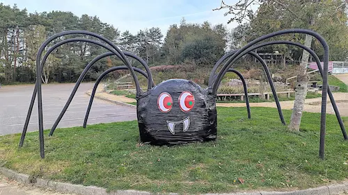 Large black spider decoration with red eyes and long curved legs on grass.