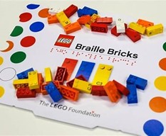 A selection of brightly coloured LEGO Braille Bricks scattered across a card labelled “LEGO Braille Bricks, The LEGO Foundation.”