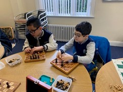 Two young boys playing chess at a wooden table.