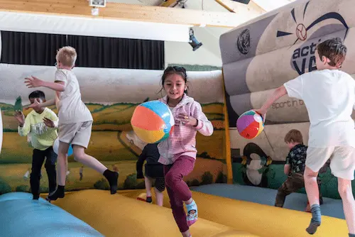 Children playing with beach balls on an inflatable activity area indoors.