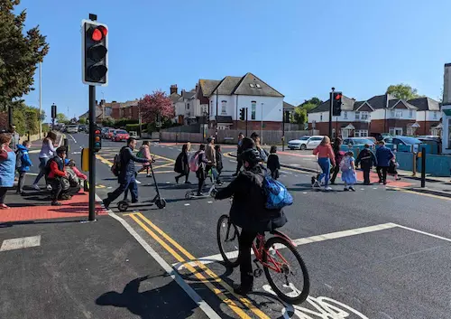 Picture of many children using a pedestrian crossing to travel to school.  