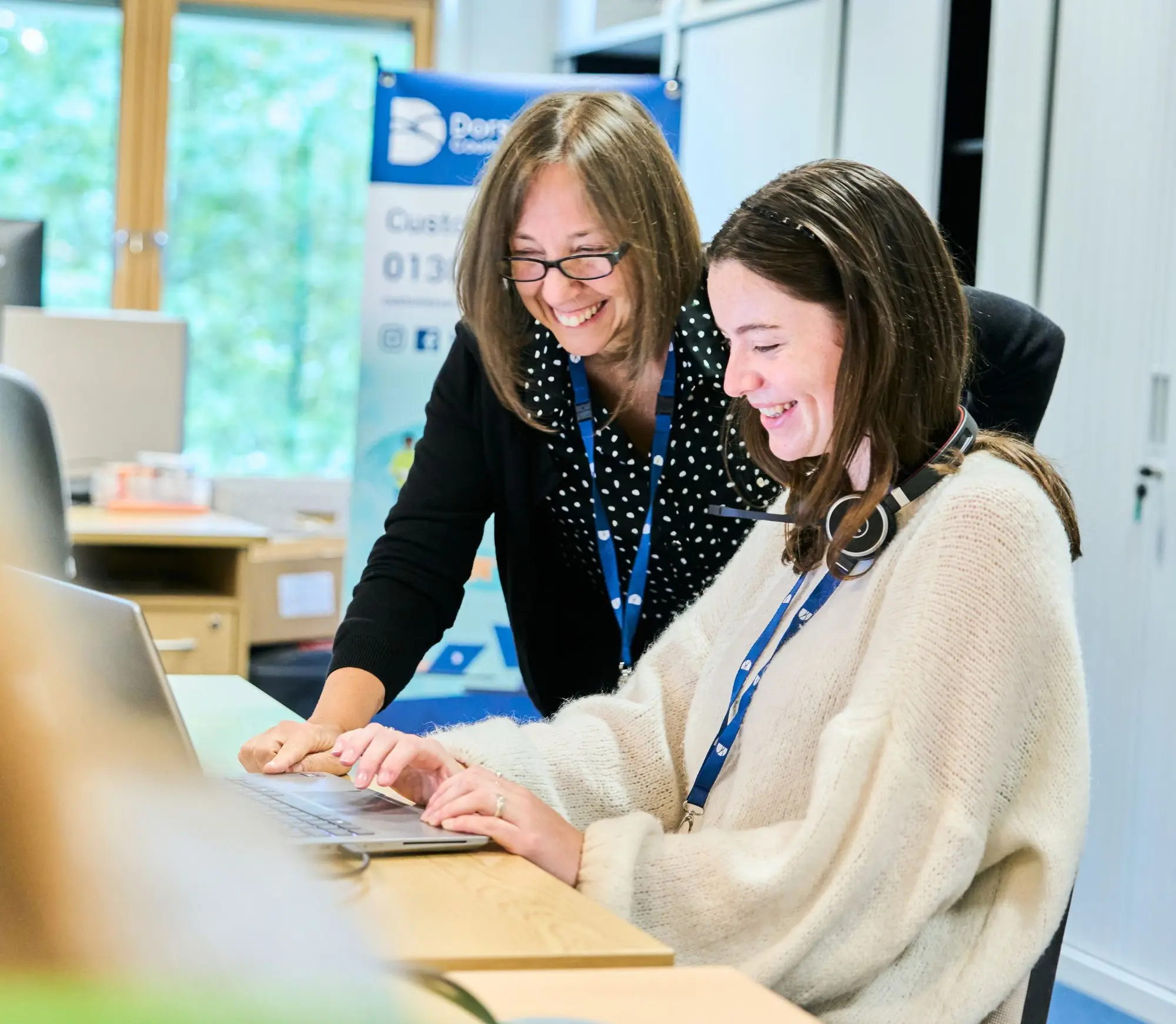 Two colleagues sat at a laptop smiling