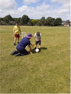 A child being coached on how to play cricket by a man kneeling down. They are outside in a green field.