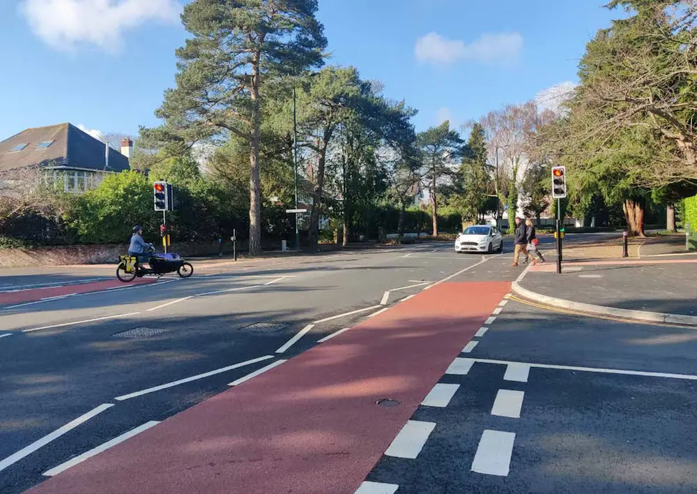 View of cycle lane and crossing on the highway at Glenferness Avenue, Bournemouth as part of Transforming Travel corridor. Picture includes people crossing the road, a car and cyclist with front carriage for a child to accompany.