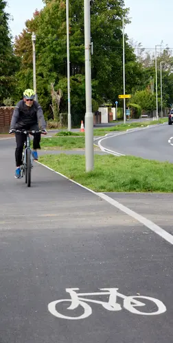 Cyclist using a segregated cycle lane alongside a road on Wimborne Road, with trees and grass verges alongside the route.